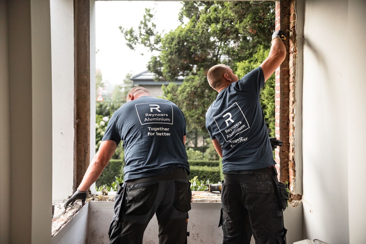 Deux installers de Reynaers Aluminium démontent d’anciennes fenêtres sur place.