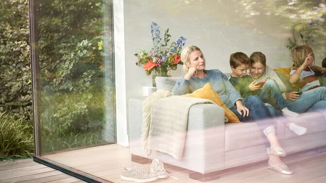 Women with children sitting in sofa behind large window wall.