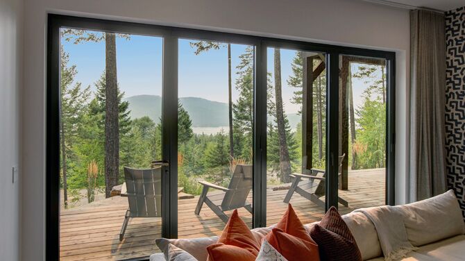 Living room with broad folding doors in the background, looking out on green woods.