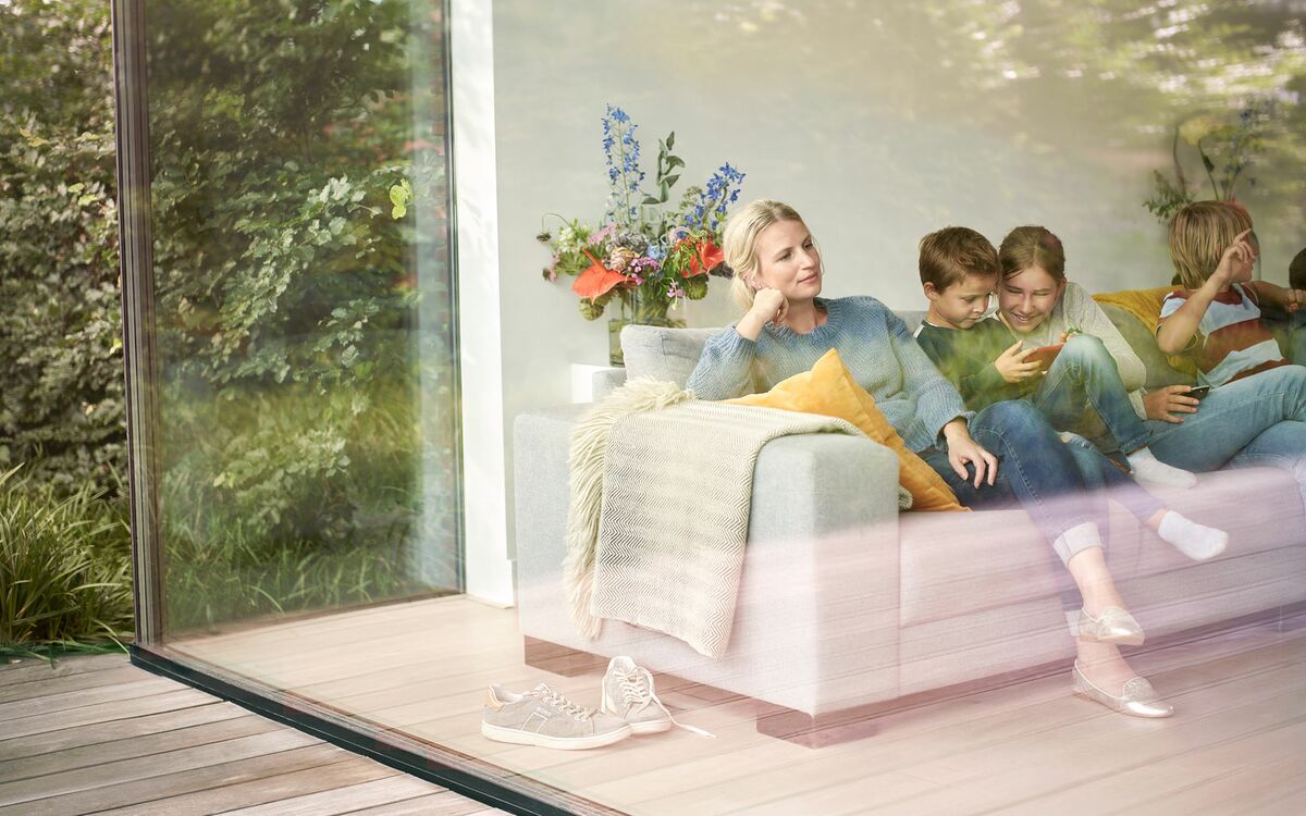 Woman relaxing with children on couch behind large glass surface.