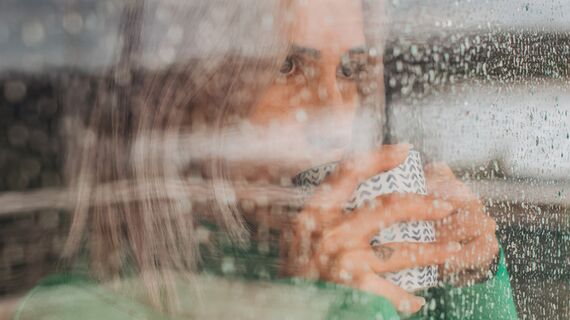 Woman drinking coffee behind glass window on a rainy day.