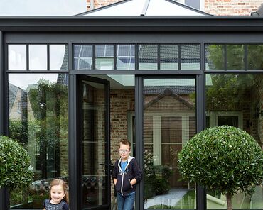 Children playing in the garden in front of black Reynaers Aluminium conservatory.